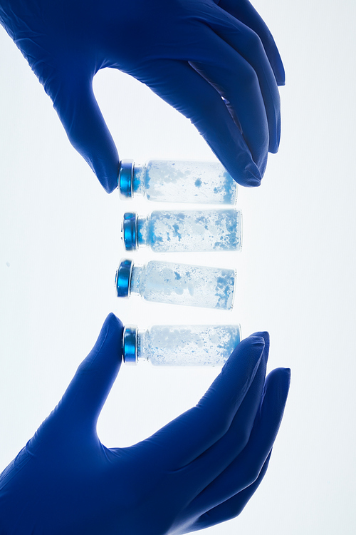 Top view background of gloved hands holding glass vials in row over white table in medical laboratory, copy space
