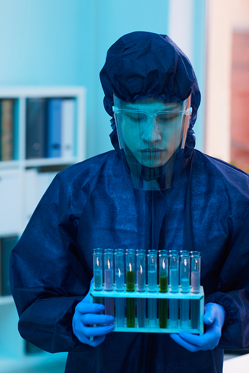 Vertical portrait of scientist in full protective costume holding test tubes while working on research in laboratory