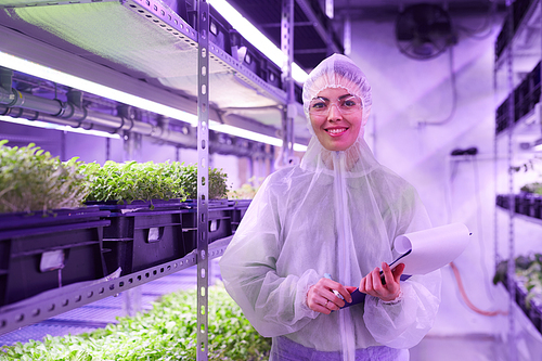 Portrait of female agricultural engineer smiling happily at camera while posing in plant  greenhouse lit by blue light, copy space