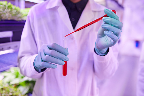 Mid section crop of unrecognizable scientist holding glass tube with red liquid while working in bio laboratory, copy space