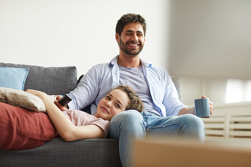 Portrait of happy couple watching TV together while sitting on sofa at home in cozy apartment enjoying  time, copy space