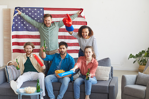 Multi-ethnic group of friends watching sports match and cheering emotionally while holding American flag, copy space