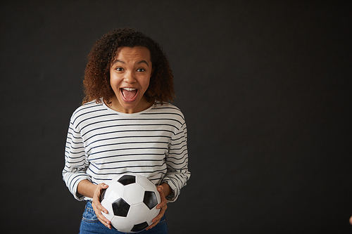 Waist up portrait of excited African-American girl holding football ball while posing against black background and  , copy space