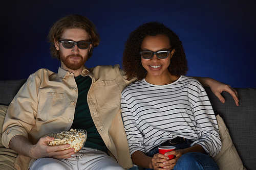 Portrait of mixed-race modern couple watching movie and wearing stereo glasses while enjoying date in cinema