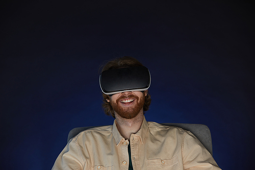 Head and shoulders portrait of adult bearded man wearing virtual reality gear while enjoying immersive videogame or movie in dark