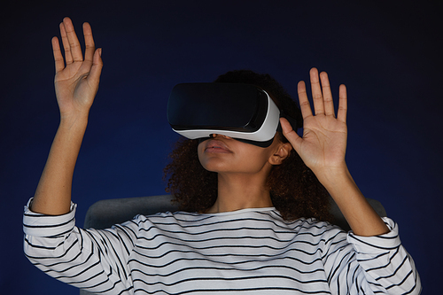 Portrait of mixed-race young woman wearing virtual reality gear while enjoying immersive videogame or movie in dark