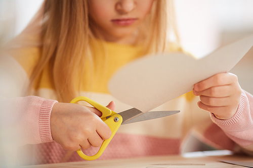 Sunlit close up of cute girl making heart-shaped holiday card for Mothers day or Valentines day while sitting at table in cozy home interior, copy space