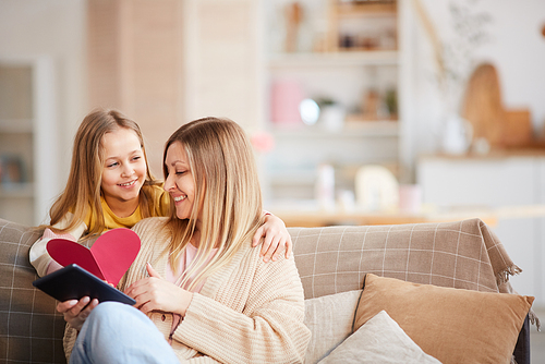 Warm toned portrait of cute little girl giving heart-shaped card to happy mother on Mothers day or Valentines day, copy space