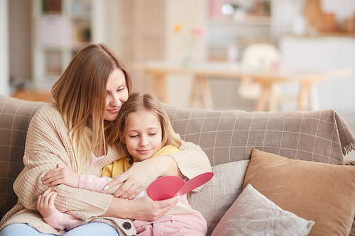 Warm-toned portrait of smiling mother embracing daughter while reading handmade card on Mothers day, copy space