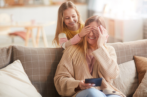 Warm toned portrait of cute girl playing peek a boo with mom while surprising her on Mothers day, copy space