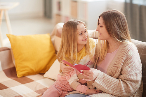 Portrait of blonde little girl embracing mom while celebrating Mothers day together sitting on cozy couch at home, copy space