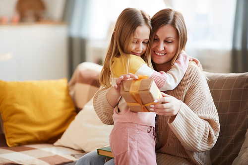 Warm-toned portrait of cute girl hugging mom after giving gift for Birthday or Mothers day, copy space