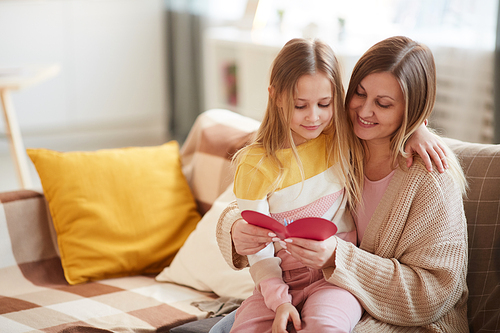 Warm-toned portrait of happy mother hugging daughter while reading holiday card on Mothers day, copy space