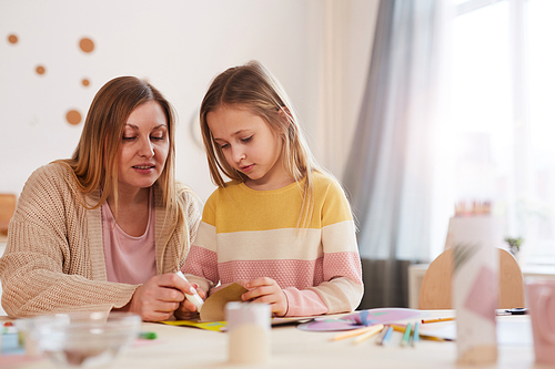 Warm-toned portrait of mature mother enjoying art and crafts with cute daughter in home interior, copy space