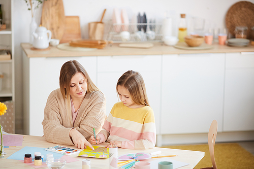 High angle portrait of mature mother helping cute daughter with art and craft project in home interior, copy space