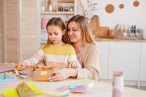 Warm-toned portrait of happy mother hugging daughter while opening presents at wooden kitchen table