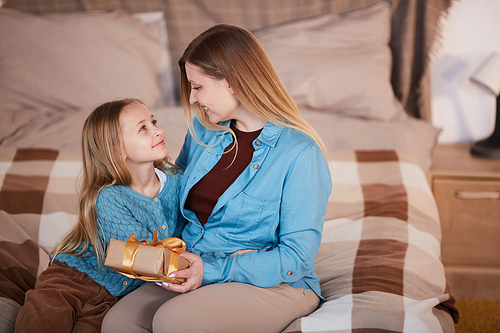 High angle portrait of happy mother hugging cute girl and smiling at each other while opening present sitting on bed, copy space