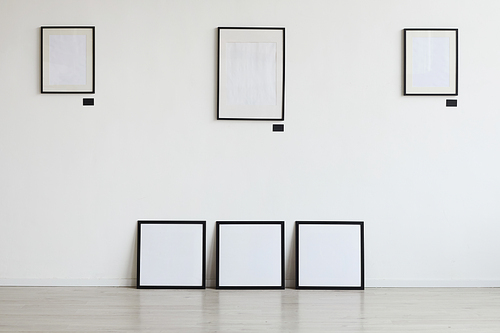 Background image of empty black frames hanging on white wall at art gallery, copy space
