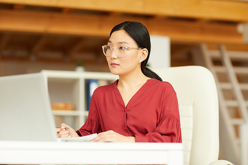 Portrait of successful Asian woman wearing red blouse working at desk in modern white office, copy space