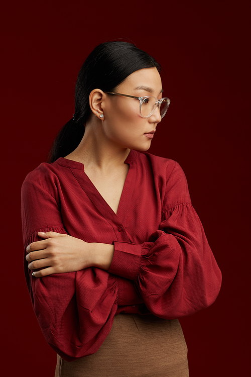 Waist up portrait of Asian woman wearing red blouse posing stiffly against maroon background in studio