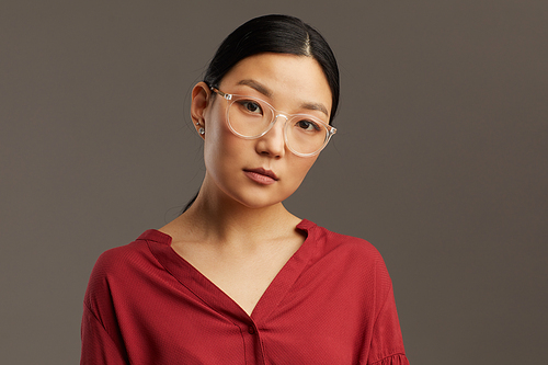 Head and shoulders portrait of elegant Asian woman wearing glasses and  while standing against grey background in studio, copy space