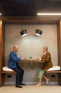 Side view full length portrait of two people sitting at table in indoor cafe during business meeting, copy space