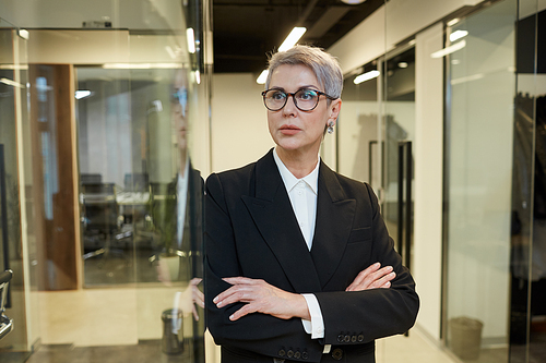 Waist up portrait of successful mature woman standing with arms crossed in modern office interior, copy space