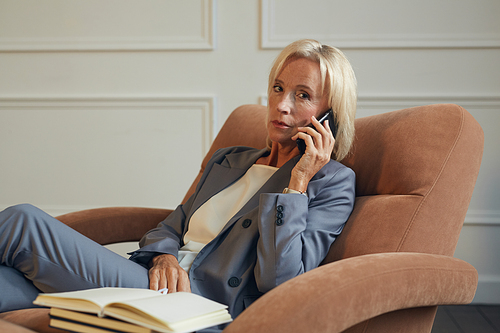 Minimal portrait of successful mature businesswoman  while speaking by phone in lounge chair in office, copy space