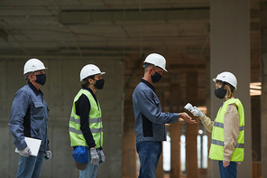 Side view of female supervisor measuring temperature of workers with contactless thermometer pointing at hands, copy space
