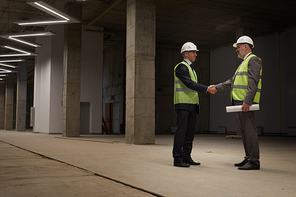 Full length portrait of two successful business people shaking hands while standing at construction site, copy space
