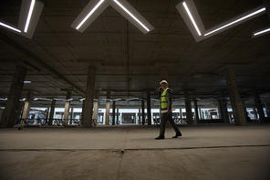 Wide angle view of mature businessman wearing hardhat and speaking by phone while walking across construction site indoors, copy space