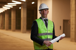 Waist up portrait of mature businessman wearing hardhat and  while standing at construction site indoors, copy space