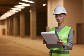 Waist up portrait of mature female worker wearing hardhat and  while standing at construction site indoors, copy space