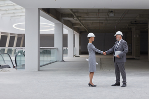 Full length side view portrait of smiling businesswoman shaking hands with partner after investment deal at construction site, copy space