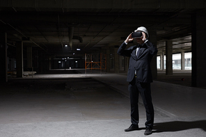 Dark full length portrait of businessman wearing VR gear at construction site while visualizing future project in 3D, copy space