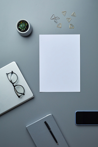 Above view flat lay of blank white paper on grey workplace background with smartphone and business accessories, copy space