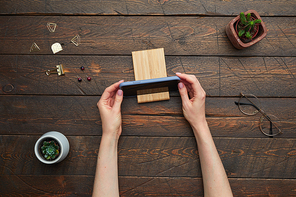 Minimal above view flat lay of female hands putting smartphone on stand over textured wooden workplace background, copy space