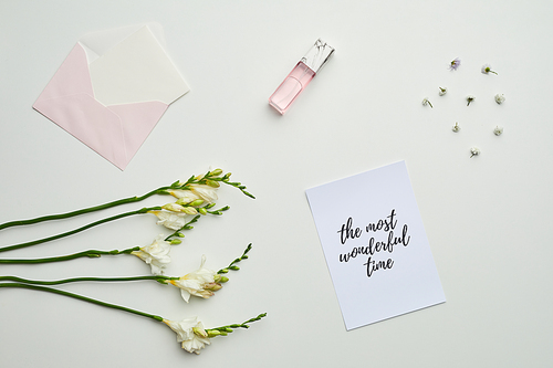 Minimal background composition of envelope and perfume on table with floral details and lettering the most wonderful time, copy space