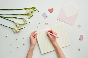 Minimal background composition of female hands writing in planner against while table background with floral decor, copy space
