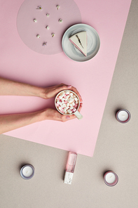 Minimal composition of female hands holding cup of sweet cocoa over pink graphic background, copy space
