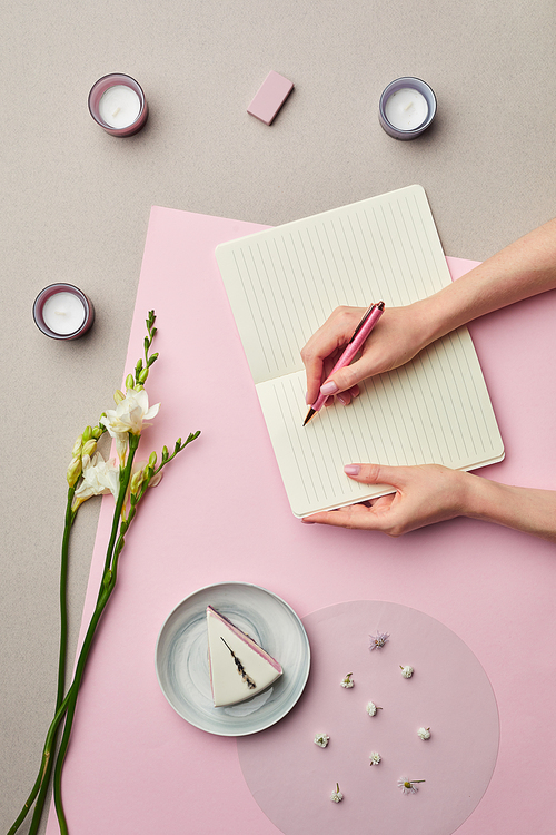 Minimal composition of female hands writing in blank planner over pink graphic background with floral decor, copy space