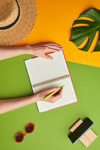 Bright color pop composition of female hands writing in planner over graphic tropical background with vacation vibes, copy space