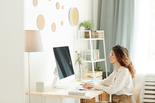 Young adult businesswoman working on modern computer while staying at home, horizontal side view shot