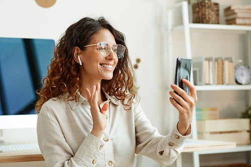 Beautiful Caucasian businesswoman wearing stylish eyeglasses having video call on her smartphone, horizontal portrait