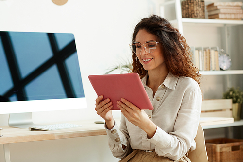 Horizontal medium portrait of young businesswoman wearing eyeglasses using tablet computer for work