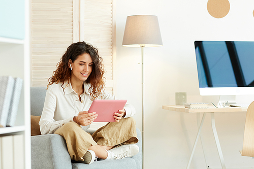 Young woman sitting relaxed in her armchair and working using tablet computer and Internet