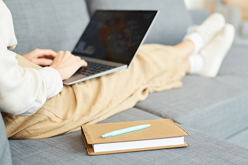 Unrecognizable woman sitting relaxed on sofa at home working on her laptop, horizontal shot