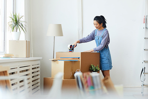 Side view portrait of young Asian woman packing cardboard boxes and smiling happily while moving to new home or apartment, copy space