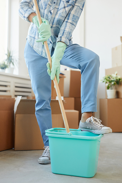 Vertical low section portrait of cheerful young woman cleaning new house or apartment while moving in