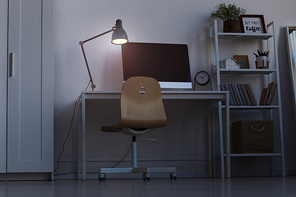 Full length background image of home office workplace at night, with focus on computer desk lit by dim lamp light, copy space